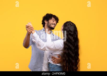 Loving indian couple holding hands and dancing, hugging and smiling at each other while having date, yellow background Stock Photo