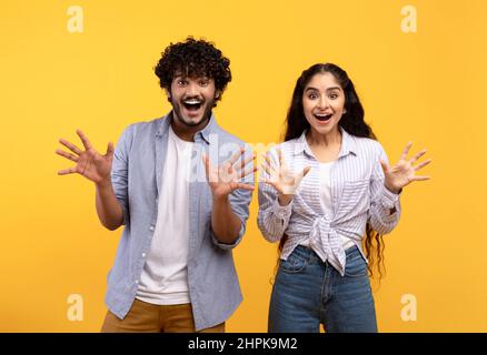 Emotional indian couple gesturing together, having surprised face expressions and showing amazement, yellow background Stock Photo