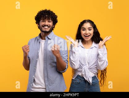 Wow. Overjoyed indian spouses gesturing in amazement looking at camera over yellow studio background Stock Photo