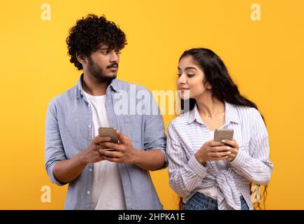 Shocked indian woman spying on her boyfriend using smartphone, texting sms or scrolling social media news feed Stock Photo