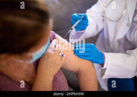 High angle view of caucasian mature female doctor vaccinating caucasian mature woman at home Stock Photo