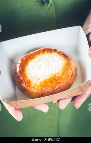 Cheesy brioche bun or vatrushka in a craft paper box. Take away food concept. Stock Photo