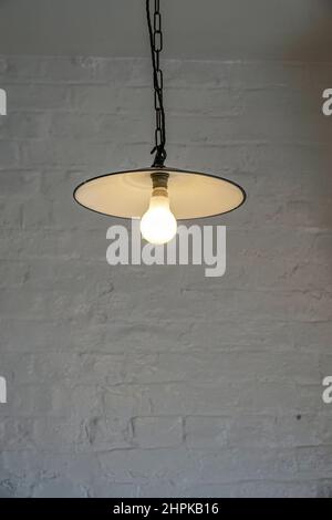 Single light hanging from the ceiling against a brick wall Stock Photo