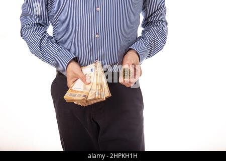 male hands holding Euro banknotes and one Bitcoin coin on a white background. Euro Money or Bitcoin cryptocurrency investing concept. Stock Photo