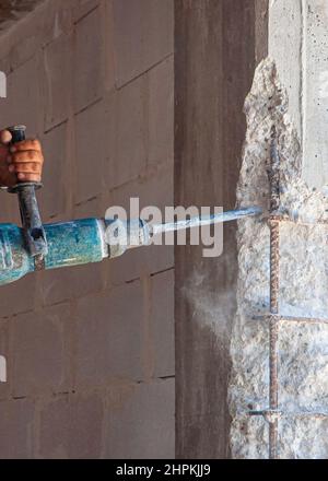 Builder worker pneumatic hammer drills hole in concrete brick wall with diamond crown for electric cable, socket, switch. Stock Photo