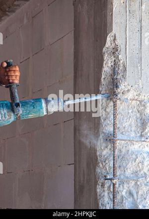 Builder worker pneumatic hammer drills hole in concrete brick wall with diamond crown for electric cable, socket, switch. Stock Photo