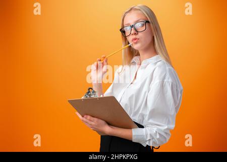 Teen school girl taking notes on clipboard against orange background Stock Photo