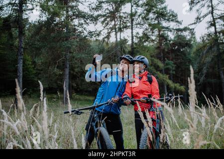 Senior couple bikers using smartphone outdoors in forest in autumn day. Stock Photo