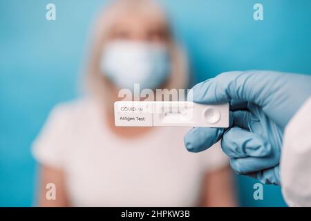 Doctor in protective suit medical mask gloves hand holding new rapid lateral flow COVID 19 tests over bright blue color background Stock Photo
