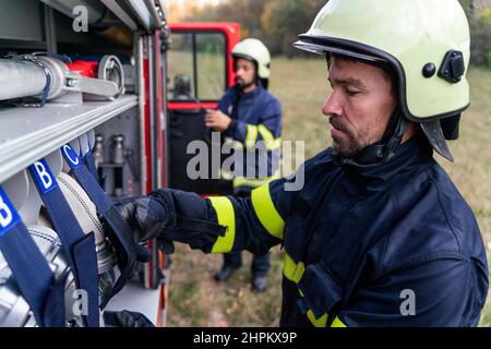Firefighters men taking an oxygen mask from fire truck outdoors in nature. Stock Photo