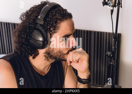 closeup of caucasian young man touching his lips thinking and staring, inside his home recording studio, music industry concept. Stock Photo