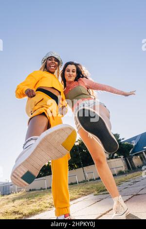 Kicking the air with bestie. Two female best friends friends having fun while standing together outdoors in the city. Happy female youngsters feeling Stock Photo