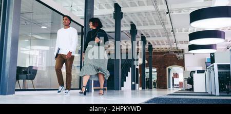 Two businesspeople walking together in an office. Two business colleagues talking to each other on the move. Confident businesspeople working together Stock Photo