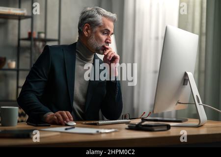 Mature businessman working on computer indoors in office. Stock Photo