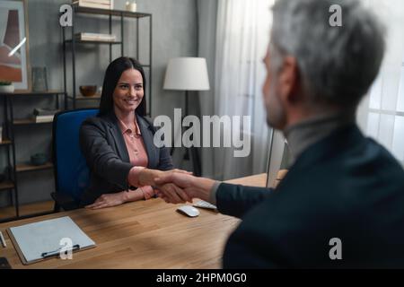 A financial advisor shaking hand with her client indoors in office. Stock Photo