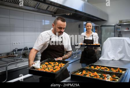 Chef and cook working on their dishes indoors in restaurant kitchen. Stock Photo