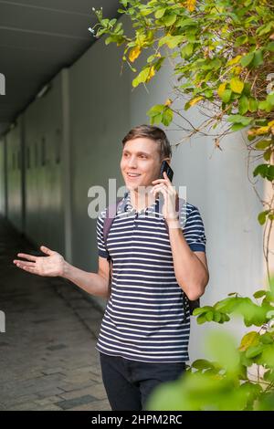 Portrait of young caucasian man in casual clothes standing outdoors and making phone call. Using smartphone, talking by the phone. Urban lifestyle. Stock Photo