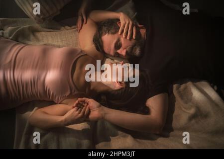 Overhead view of mid-adult couple lying in bed at night and hugging and looking at each other. Stock Photo