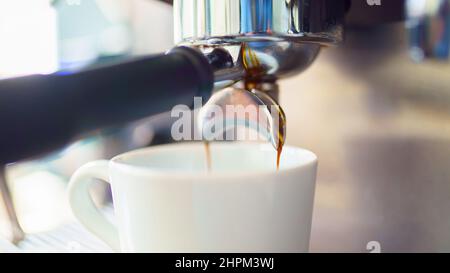 espresso coffee is pouring from the coffee machine into a white cup Stock Photo