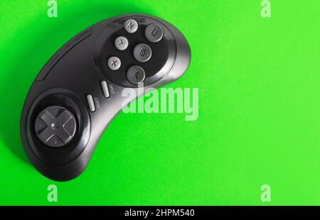 Close up photo of classic wireless black colored 16 bit game pad controller laying on green background. Stock Photo
