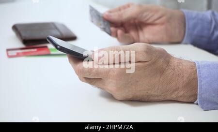 The hands of a man who, holding a smartphone, a credit card, makes a successful payment. Stock Photo