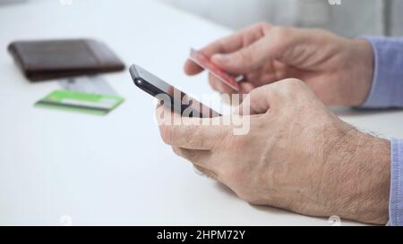 The hands of a man who, holding a smartphone, a credit card, makes a successful payment. Stock Photo