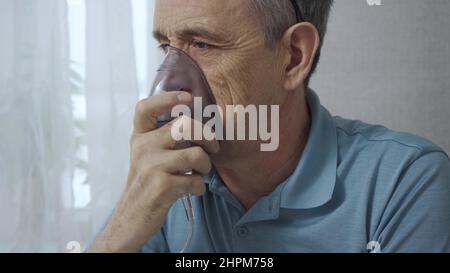 An elderly man is using an inhaler. Treatment of airway inflammation with a nebulizer. Close-up. Rehabilitation after illness Stock Photo
