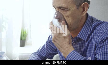 An elderly man is using an inhaler. Treatment of airway inflammation with a nebulizer. Close-up. Rehabilitation after illness Stock Photo