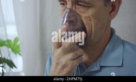 An elderly man is using an inhaler. Treatment of airway inflammation with a nebulizer. Close-up. Rehabilitation after illness Stock Photo