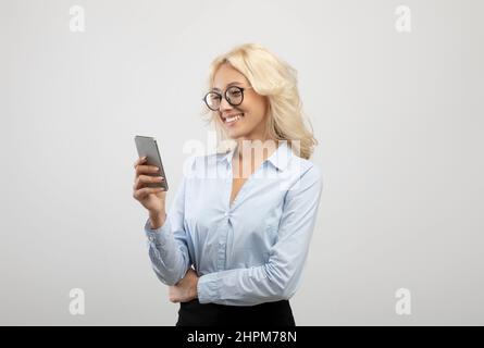 Portrait of young female entrepreneur with cellphone working online or chatting with client over light studio background Stock Photo