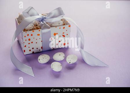 Easter creative layout with Easter eggs in a gift box with lavender blush ribbons on pale purple background Stock Photo