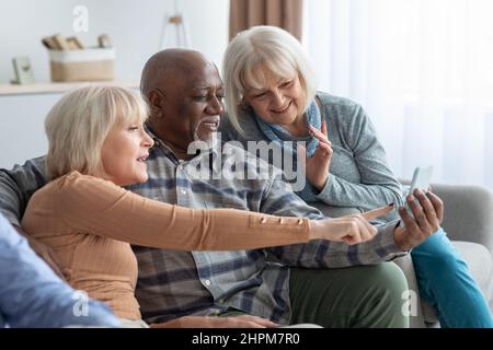 Cheerful elderly people spending time together at home, using smartphone Stock Photo
