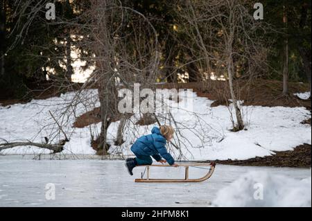 Toddler boy in winter suit having fun outside in snowy nature with a sledge on natural ice. Stock Photo