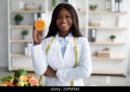 Vitamin C is good for immunity. Happy african american dietologist holding orange half, recommending fresh fruits to eat Stock Photo