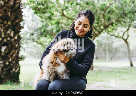 Cute young woman is hugging her little puppy. Love between owner and dog. Outdoor photo in the park, selective focus. Lifestyle concept Stock Photo