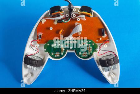 Photo of classic disassembled wired modern silver colored game pad controller laying on blue background. Stock Photo