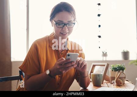 Welcome to the digital age. Cropped shot of an attractive young businesswoman sitting alone in her home office and texting on her cellphone. Stock Photo