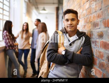 Friends make college fun. Portrait of a handsome young male student leaning against a wall with his friends in the background. Stock Photo