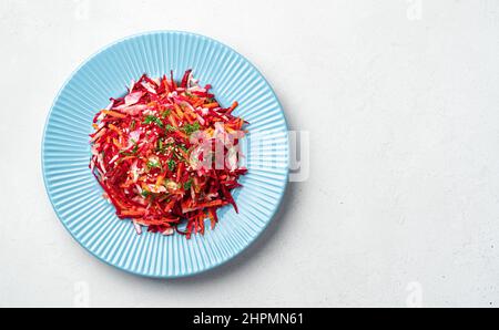 Salad of fresh vegetables with cabbage, beets, carrots and sesame seeds in a blue plate on a gray background. Cleansing, dietary salad. Top view, copy Stock Photo