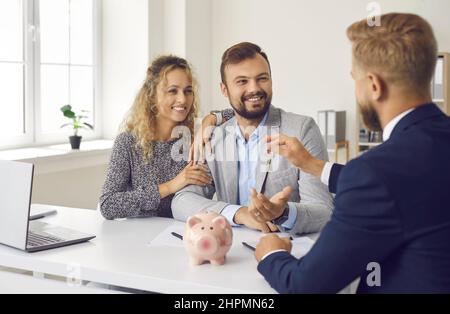 Happy young family signs contract in office and receives keys from real estate agent. Stock Photo