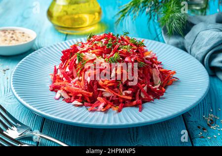 Salad with beets, carrots and cabbage seasoned with parsley and sesame seeds close-up on a blue background. Side view. Healthy food. Stock Photo