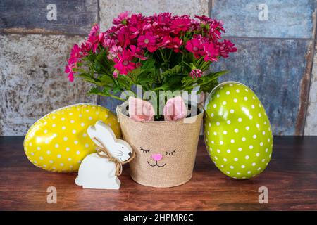 Flowerpot with a rabbit's face, a wooden Easter bunny and two cardboard Easter eggs in focus. Stock Photo