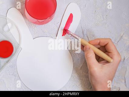 female hand paints a paper easter bunny with red paint. Stock Photo