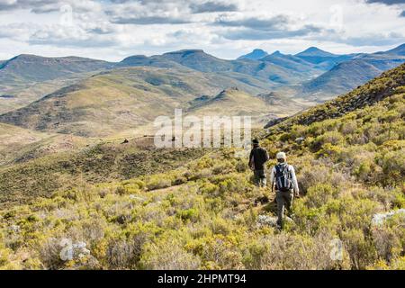 Travel to Lesotho. 2 hikers in the mountains with the shepherds' huts in the distance Stock Photo