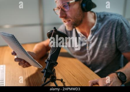 Microphone with pop filter closeup photo with blogger man in headphones recording voice or making online webinar or news announcement. Modern home sou Stock Photo