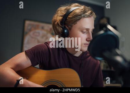 Home sound studio young teenager portrait playing guitar in Headphones and recording music using microphone. Modern audio recording technology concept Stock Photo