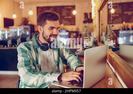 Cheerful bearded man working on laptop in cafeteria Stock Photo