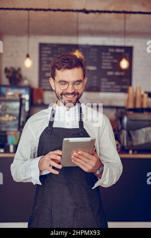 Cheerful man barista using tablet computer in cafe Stock Photo