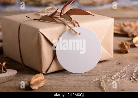 Round white gift tag mockup on Christmas or Valentines Day wrapped presents on rustic wooden background with boho decoration. Spring blank label produ Stock Photo
