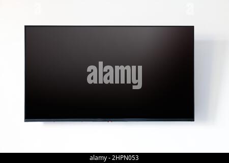 TV blank LED screen on white wall background. Black empty television display front view, copy space, mock up template Stock Photo